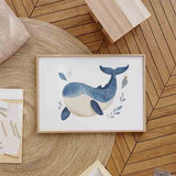Cuadro horizontal con ballena azul infantil, vientre crema, hojas marinas azules, fondo blanco y composición suave de estilo infantil. Disponible en kudeko.com