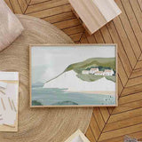 Horizontales Wandbild mit Küstenlandschaft, weißen Klippen, sanft blau grauem Meer, grünen Hügeln, hellen Häusern und Illustrationsstil in weichen Pastelltönen. Erhältlich auf kudeko.com