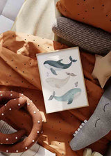 Cuadro con tres ballenas en tonos azul grisáceo, beige y celeste sobre fondo claro, con pequeñas hojas marinas y estilo infantil sereno. Disponible en kudeko.com