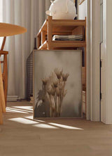 Cuadro minimalista con flores secas iluminadas por luz natural, proyectando sombras suaves sobre fondo neutro. Disponible en kudeko.com.