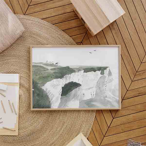 Cuadro horizontal de acantilados blancos junto al mar, colinas verdes suaves, casas lejanas y aves en el cielo, en estilo infantil. Disponible en kudeko.com
