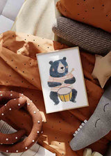 Tableau encadré avec ours enfant au pelage bleu foncé jouant un tambour jaune, t-shirt à rayures corail et blanches, fond clair et style illustré doux pour chambre d’enfant. Disponible sur kudeko.com