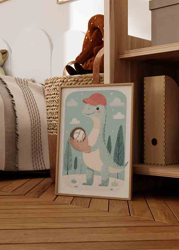 Quadro com dinossauro infantil, luva e bola de basebol, boné vermelho, fundo azul claro, nuvens brancas, árvores estilizadas e estilo suave em tons de creme, rosa e verde acinzentado. Disponível em kudeko.com