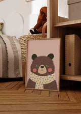 Gerahmtes Wandbild mit braunem Bären, rosigen Wangen, grünen Augen, weißem Schal mit senfgelben Punkten, sanft rosa Hintergrund und kindlichem Stil fürs Babyzimmer. Erhältlich auf kudeko.com