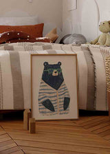 Gerahmtes Wandbild mit schwarzem Bären, grüner Brille, rosigen Wangen und blau grau gestreifter Jacke vor hellem Hintergrund, im kindlichen nordischen und modernen Stil. Erhältlich auf kudeko.com