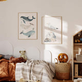 Cuadro con tres ballenas en tonos azul grisáceo, beige y celeste sobre fondo claro, con pequeñas hojas marinas y estilo infantil sereno. Disponible en kudeko.com