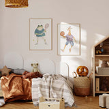 Gerahmtes Wandbild mit Giraffe beim Basketball, orangem Ball, lila Trikot, blauer Hose, weißem Hintergrund und kindlichem Stil in sanften Farben. Erhältlich auf kudeko.com