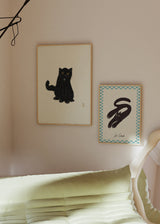 Cuadro de gato negro sentado con ojos ámbar, fondo beige claro y composición sencilla, de estilo animales. Disponible en kudeko.com
