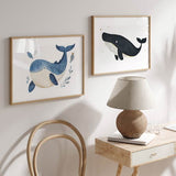 Cuadro horizontal con ballena azul infantil, vientre crema, hojas marinas azules, fondo blanco y composición suave de estilo infantil. Disponible en kudeko.com