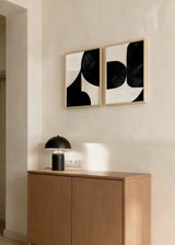 Set aus zwei Wandbildern mit geschwungenen abstrakten schwarzen Formen auf hellbeigem Hintergrund, moderne kontrastreiche Komposition im minimalistischen Stil für stilvolle Wandgestaltung. Erhältlich auf kudeko.com