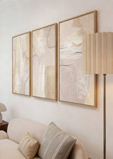 Conjunto de três quadros com composição abstrata em tons marfim, bege, areia e cinzento claro, linhas orgânicas, texturas suaves e estilo contemporâneo depurado. Disponível em kudeko.com