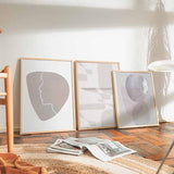 Tableau encadré avec silhouette de visage en ligne blanche continue sur forme organique beige, sable et gris doux, dans un style minimaliste et épuré. Disponible sur kudeko.com