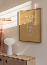 Cuadro con frase HOME IS WHERE THE LOVE IS en letras blancas sobre fondo beige cálido y corazón lineal fino, de estilo con frases. Disponible en kudeko.com