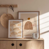 Quadro emoldurado com arco-íris repetidos em bege, areia e terracota suave sobre fundo creme, num estilo infantil moderno e equilibrado para quarto de bebé ou canto de brincadeira. Disponível em kudeko.com
