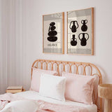 Ensemble de deux tableaux avec pierres empilées, vases noirs aux formes organiques, fond beige chaud et style minimaliste pour une décoration murale sobre. Disponible sur kudeko.com