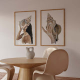 Quadro com uma mão a segurar uma grande concha marinha sobre fundo branco, em tons de bege, areia, castanho e marfim, num estilo de ilustração limpo e natural. Disponível em kudeko.com