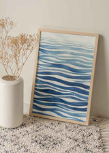 Quadro emoldurado com linhas onduladas em azul-marinho, azul médio e azul-claro sobre fundo branco, composição abstrata inspirada no movimento da água e num estilo marítimo sereno. Disponível em kudeko.com