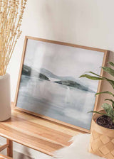 Horizontales gerahmtes Wandbild mit Küstenlandschaft, flachen Inseln, fernen Hügeln und ruhigem Wasser in Grau, Weiß und zartem Blau, im Stil Natur und Landschaften. Erhältlich auf kudeko.com