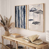 Cuadro con dos sombrillas de playa a rayas azul marino y blanco, fondo claro y composición ligera de estilo ilustración. Disponible en kudeko.com