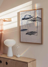 Cuadro con dos sombrillas de playa a rayas azul marino y blanco, fondo claro y composición ligera de estilo ilustración. Disponible en kudeko.com