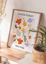 Cuadro con flores silvestres en tonos naranja, amarillo, lila y verde oliva, hojas decorativas y texto Flower Market New York, de estilo ilustración. Disponible en kudeko.com