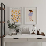 Cuadro con flores amarillas y blancas, hojas verde oliva, fondo rosa suave y tipografía decorativa, en estilo ilustración botánica alegre. Disponible en kudeko.com