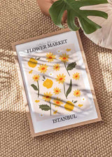 Cuadro con flores amarillas y blancas, hojas verde oliva, fondo rosa suave y tipografía decorativa, en estilo ilustración botánica alegre. Disponible en kudeko.com
