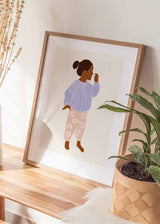 Tableau encadré avec silhouette de petite fille de profil, pull lilas, pantalon rose à fleurs blanches, fond crème et style enfantin en tons pastel. Disponible sur kudeko.com