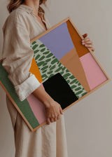 Tableau encadré avec composition abstraite de blocs irréguliers en rose, lilas, orange, vert sauge, beige et noir, avec motif organique central et style abstrait contemporain. Disponible sur kudeko.com