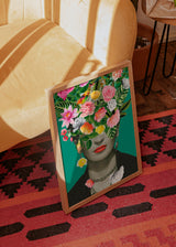 Quadro com retrato feminino a preto e branco, flores rosa, folhas tropicais verdes, ave multicolorida, lábios vermelhos, fundo turquesa e estilo floral contemporâneo. Disponível em kudeko.com