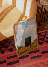Gerahmtes Wandbild mit einem Erwachsenen und einem Kind vor einem Sternenportal, goldenes Feld, blauer Himmel, weiche Wolken und surrealer Illustrationsstil in Ocker, Creme und Blau. Erhältlich auf kudeko.com