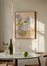 Tableau encadré avec hortensias bleu lavande et blancs dans un vase en verre, feuilles vertes, fond beige rosé et style floral délicat. Disponible sur kudeko.com