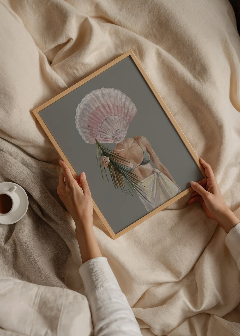 Wandbild mit weiblicher Figur im Küstenstil, großer rosa Muschel, grünem Palmblatt, Kleidung in Sandtönen, grauem Hintergrund und ruhigem Illustrationsstil. Erhältlich auf kudeko.com