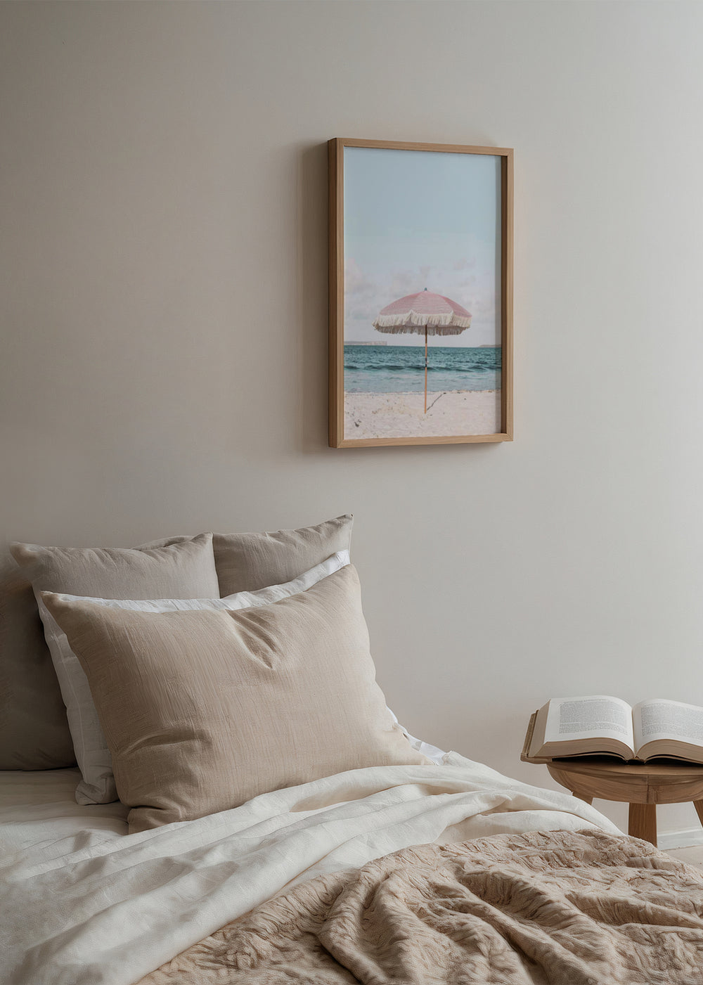 Gerahmtes Wandbild mit rosa Sonnenschirm mit Fransen auf hellem Sandstrand, ruhigem blauem Meer, pastellfarbenem Himmel und hellem Fotostil. Erhältlich auf kudeko.com
