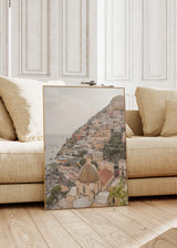 Quadro de paisagem costeira urbana de Positano com casas em socalcos, cúpula mediterrânica, mar calmo e tons areia, branco sujo, terracota e azul acinzentado, em estilo fotográfico equilibrado. Disponível em kudeko.com