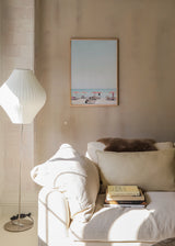 Tableau de plage avec parasols roses et orange, chaises longues blanches, sable clair, mer turquoise et style photographique lumineux au charme méditerranéen. Disponible sur kudeko.com