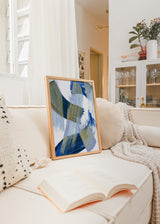 Gerahmtes Wandbild mit abstrakter Komposition aus überlagerten geschwungenen Formen in Blau, Olivbeige und Hellgrau auf weißem Hintergrund, im zeitgenössischen abstrakten Stil. Erhältlich auf kudeko.com