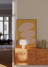 Quadro com três formas orgânicas sobrepostas em rosa claro sobre fundo mostarda, composição limpa, contraste quente e estilo abstrato para decoração de parede contemporânea. Disponível em kudeko.com