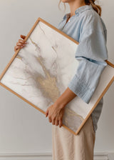 Tableau avec composition abstraite aux formes fluides en blanc cassé, gris doux et détails dorés à l’aspect minéral, style abstrait contemporain et décoration murale encadrée. Disponible sur kudeko.com