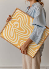 Gerahmtes Wandbild mit abstrakter Blume in Senfgelb und Weiß, wellenförmigen Linien, klarer grafischer Komposition und modernem Illustrationsstil. Erhältlich auf kudeko.com
