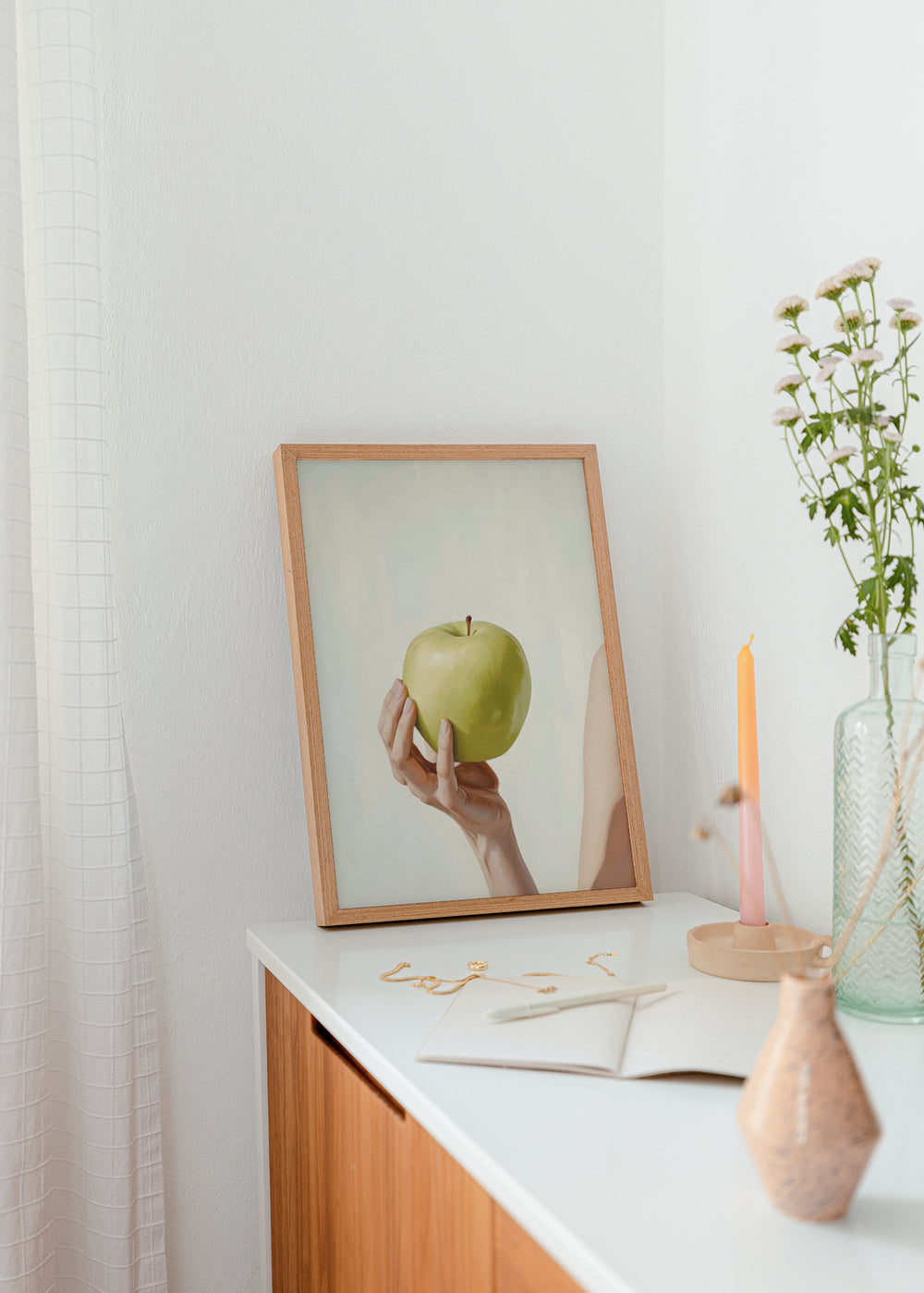 Quadro minimalista de uma mão segurando uma maçã verde. Disponível em kudeko.com.