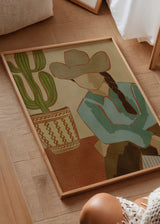 Quadro decorativo de estilo minimalista com ilustração numa sala de estar, cowgirl do deserto com cato em tons quentes, modelo Desert Cowgirl and Cactus. Disponível em kudeko.com