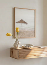 Tableau représentant une ombrelle en paille solitaire sur la plage, avec sable clair, mer beige et gris doux, et style photographique apaisant et épuré. Disponible sur kudeko.com