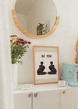 Quadro emoldurado com frase Be You, duas figuras femininas sentadas a preto sobre fundo bege claro, composição simétrica em estilo de ilustração simples. Disponível em kudeko.com