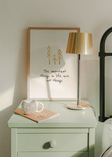 Quadro emoldurado com frase inspiradora em inglês, três árvores douradas sobre fundo branco, tipografia manuscrita preta e estilo decorativo com mensagem simples. Disponível em kudeko.com