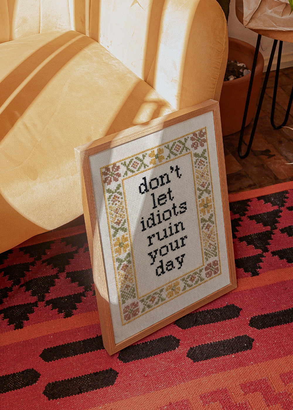 Cuadro decorativo de estilo minimalista y orgánico colocado en salón, frase bordada con humor y marco floral, modelo Don't Let Idiots Quote