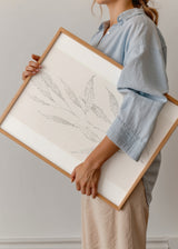 Tableau encadré avec branche de feuilles allongées en points gris sur fond beige clair, composition botanique épurée de style minimaliste pour décoration murale. Disponible sur kudeko.com