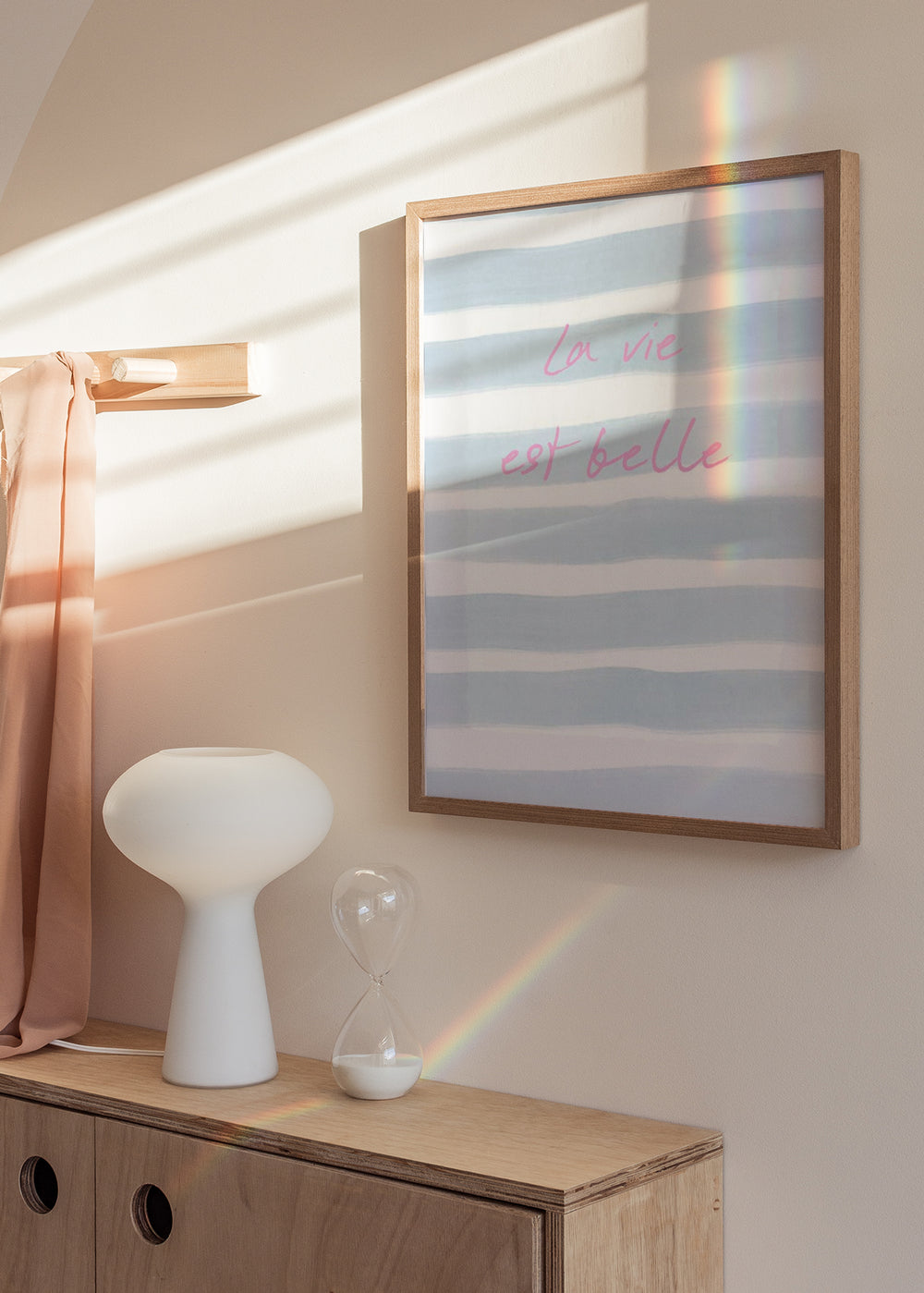 Tableau encadré avec phrase La vie est belle, rayures horizontales bleu ciel et blanches, typographie rose doux et style textuel contemporain pour chambre ou coin coiffeuse. Disponible sur kudeko.com