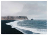Cuadro horizontal de costa con playa de arena negra, mar azul grisáceo, espuma blanca, acantilados brumosos y rocas marinas, de estilo naturaleza y paisajes. Disponible en kudeko.com