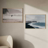 Horizontales Wandbild mit einem Surfer auf dem Weg ins Meer, zwischen weißen Wellen, nassem Sand, grauen Klippen, sanften Beigetönen und weichem Licht im fotografischen Stil. Erhältlich auf kudeko.com